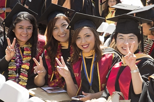 Four women in graduation caps and gowns smiling at the camera